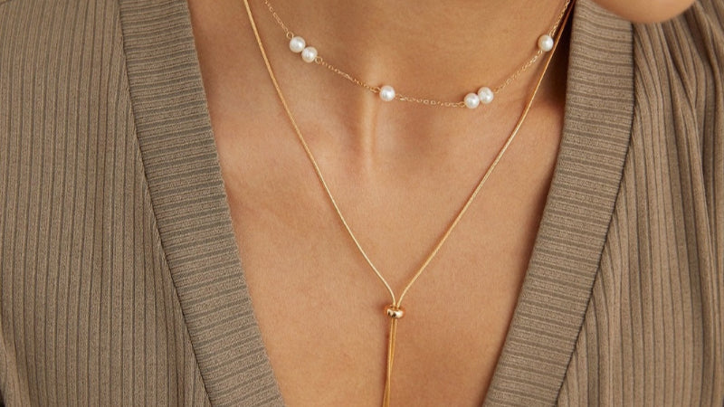 Close-up of a person wearing a gold necklace with pearl accents.